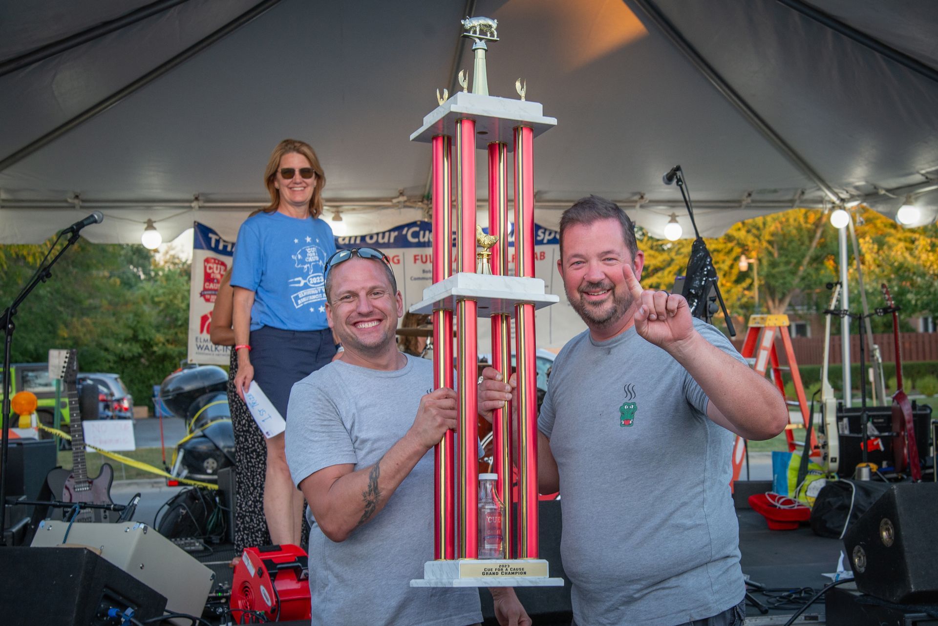 Two men are holding a trophy in a tent.