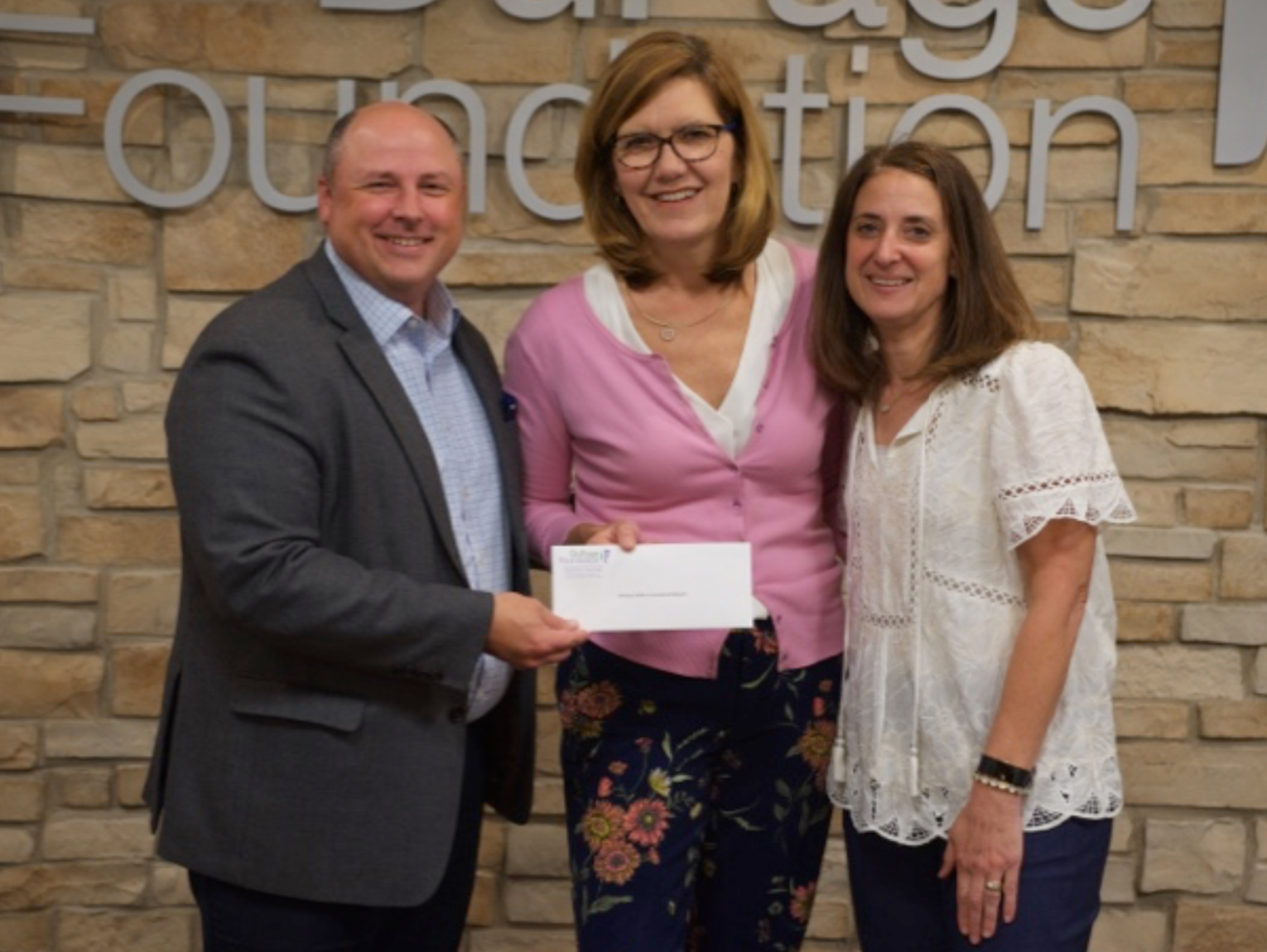 A man in a suit is handing a check to a woman in a pink shirt