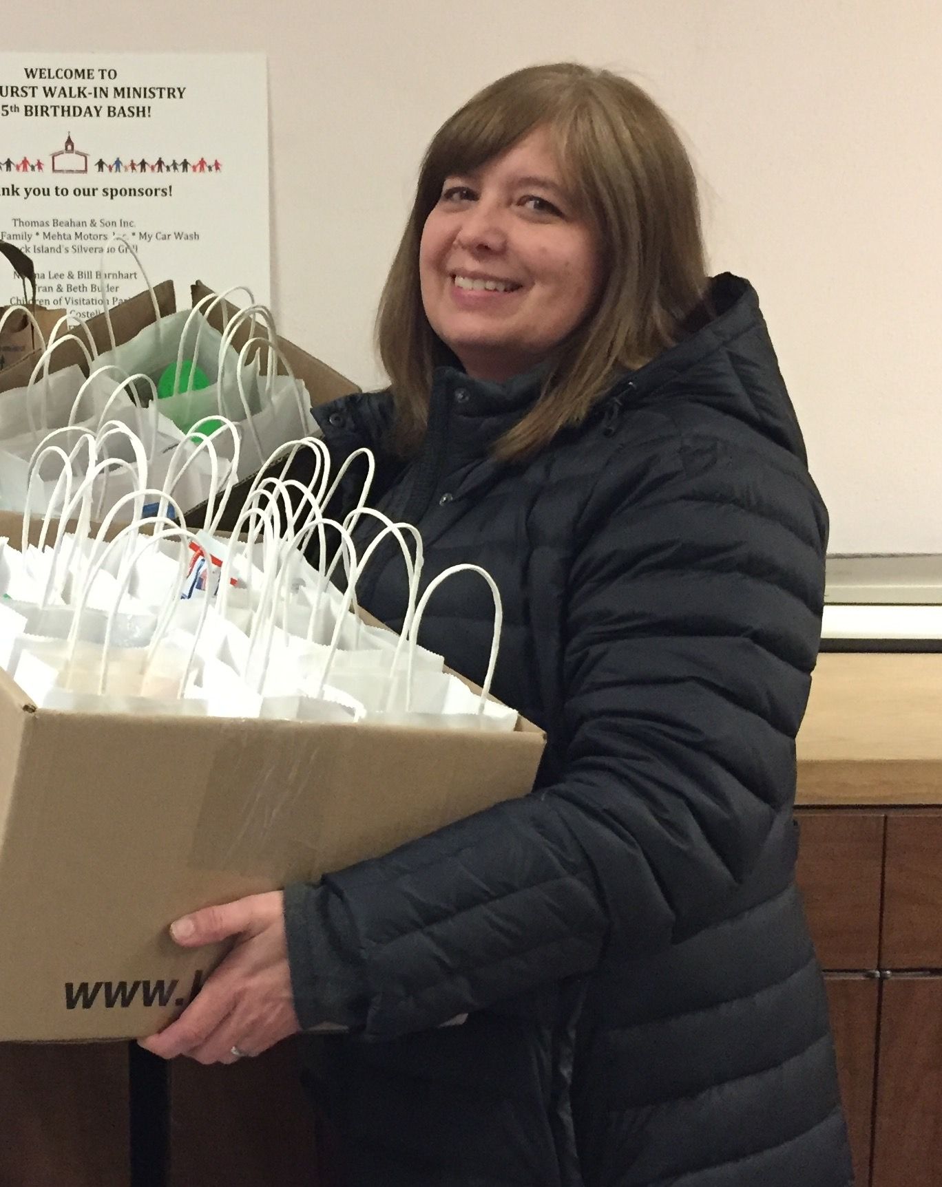 A woman in a black jacket is holding a box full of shopping bags