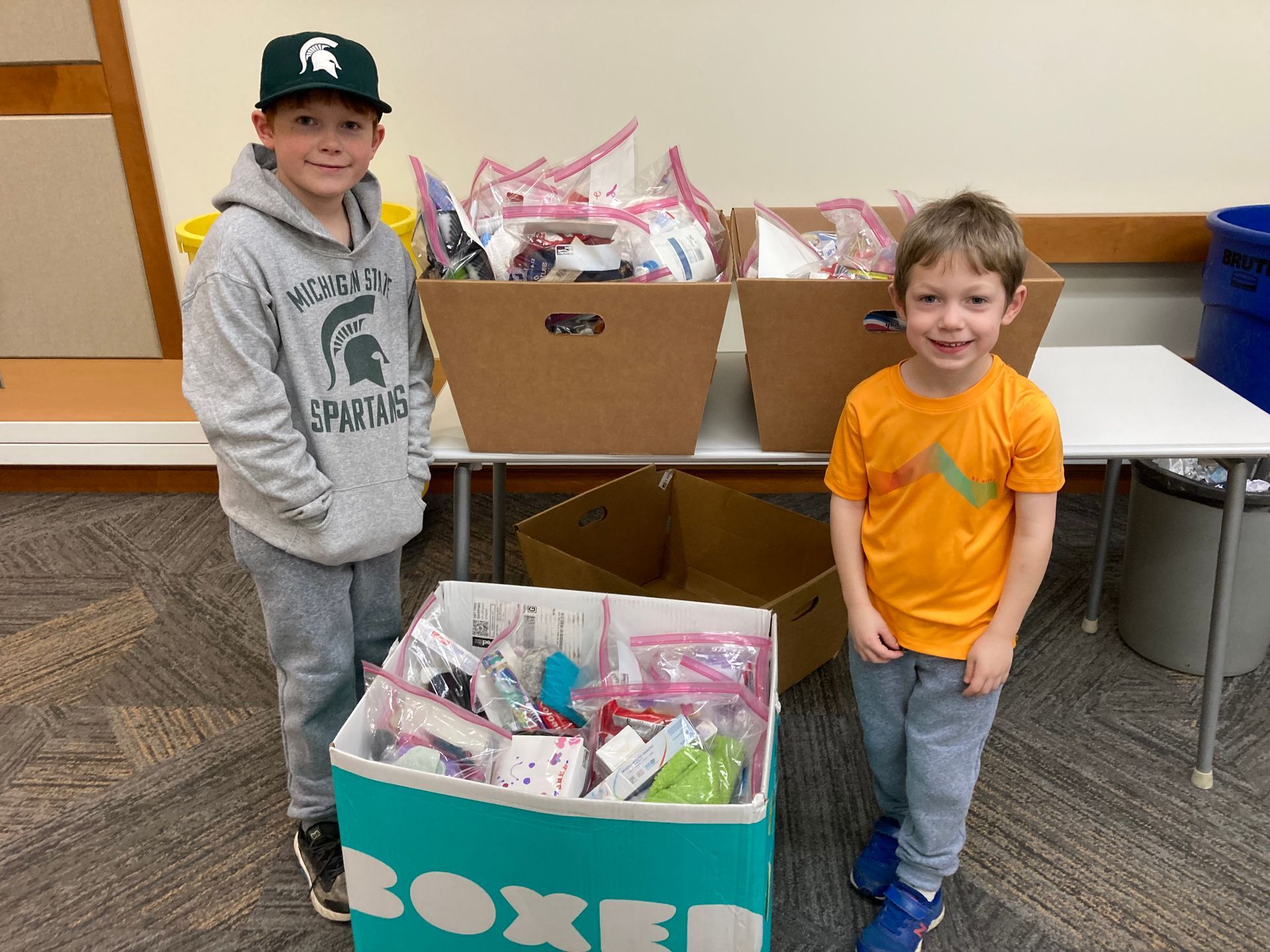 Two young boys are standing next to a box full of toys.