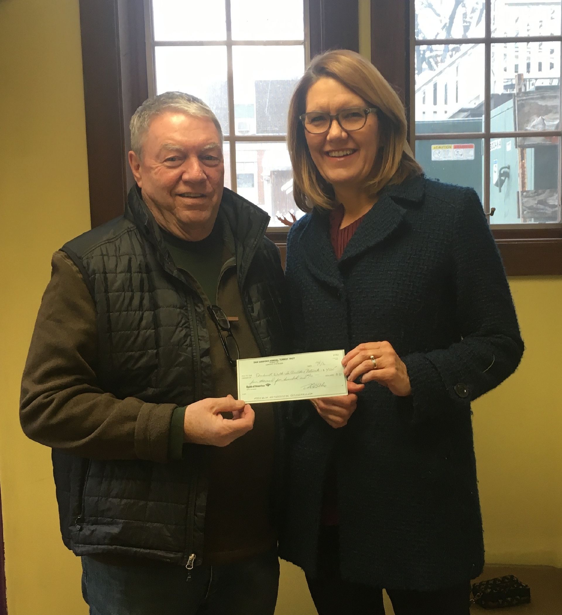 A man and a woman holding a check in front of a window