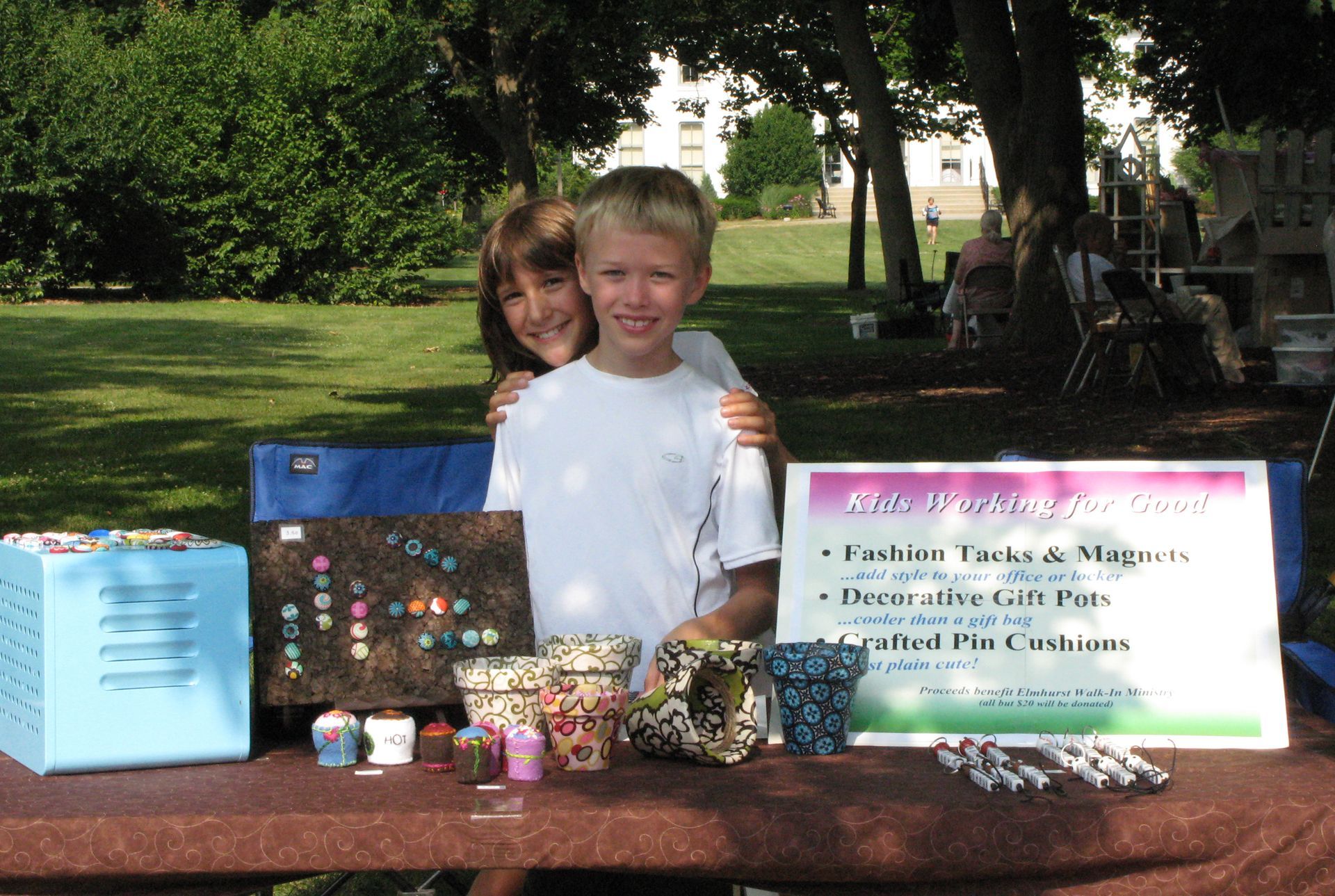 A boy and a girl are standing in front of a table with a sign that says