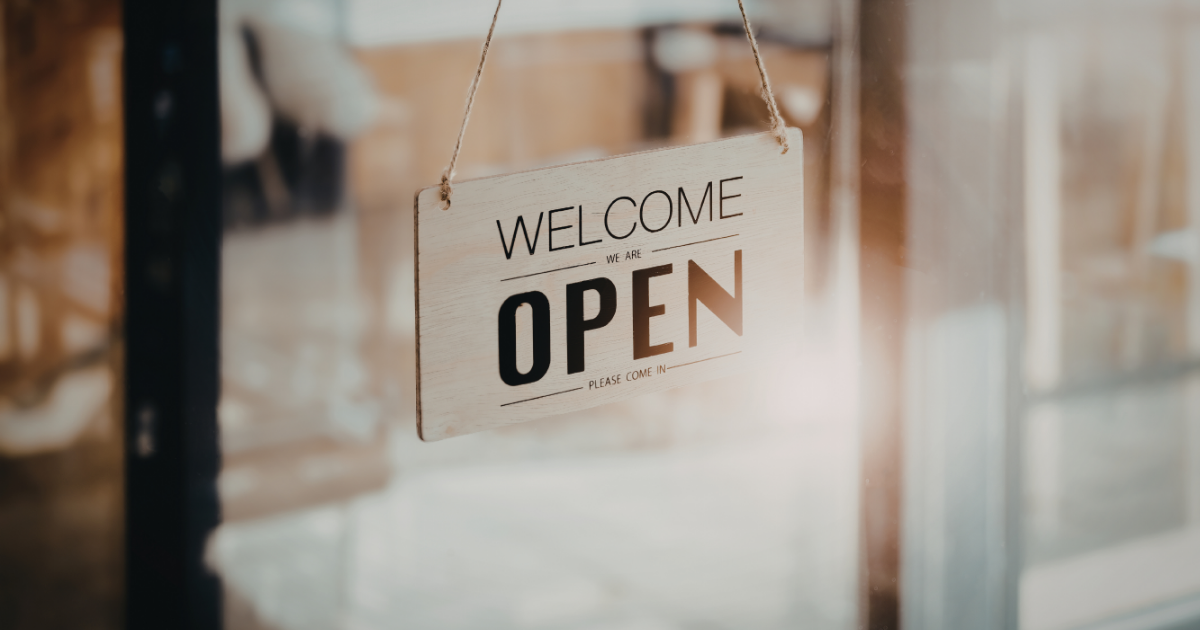 A light-colored wooden sign hangs in a glass door, reading 