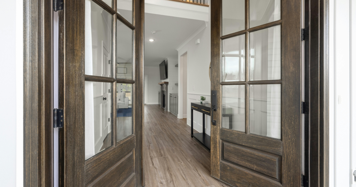 Double dark wood French doors with glass panes open into a hallway with hardwood floors and a console table.