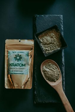 A wooden spoon filled with kratom powder next to a bag of kratom powder.