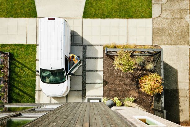 Person standing by a white van parked on a modern driveway, viewed from above.