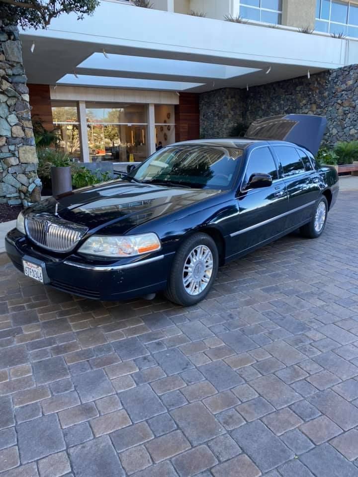 Black Lincoln Town Car limousine parked in front of a building with an open trunk.