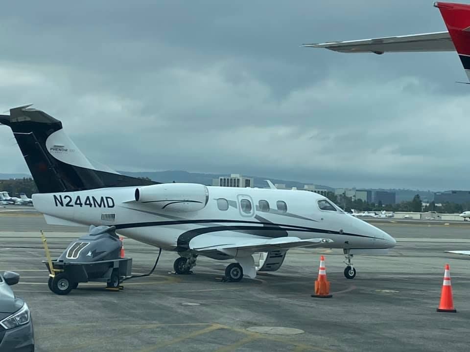 White and black private jet on a runway, N244MD, refueling, orange cones.