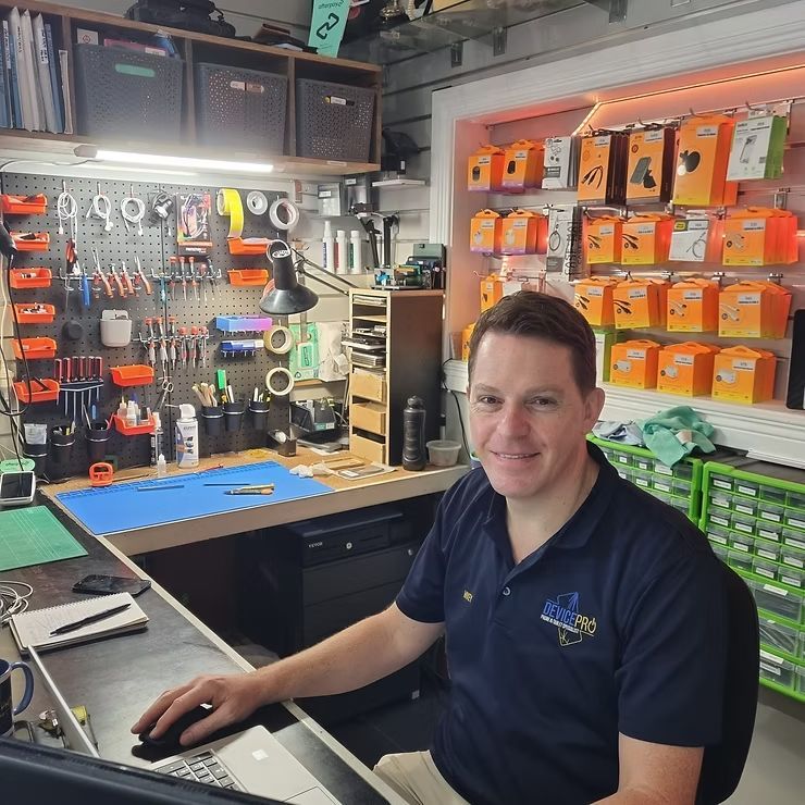 Man Seated at A Workbench in A Repair Shop, Smiling — DevicePro - Phone & Tablet Specialist In Cannonvale, QLD