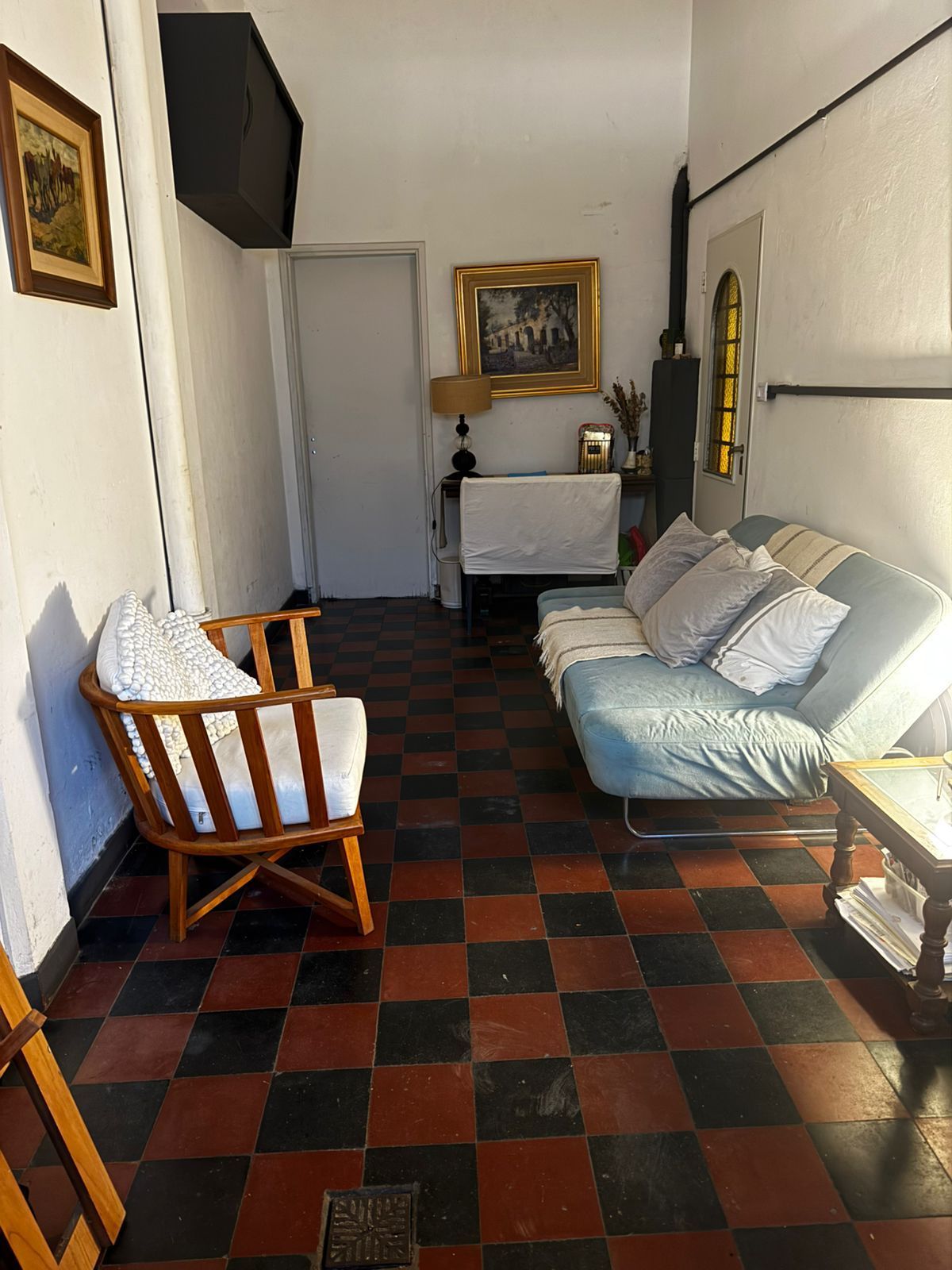 Una sala de estar con un sofá azul, un sillón de madera y un suelo de baldosas a cuadros rojas y negras.