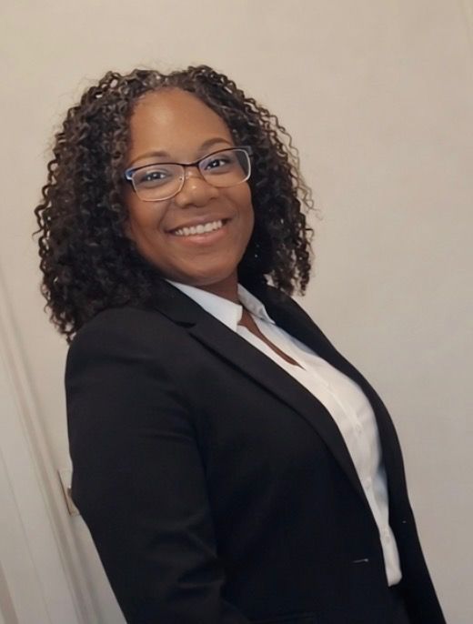 Woman in wheelchair smiles with caregiver in blue scrubs in kitchen setting.