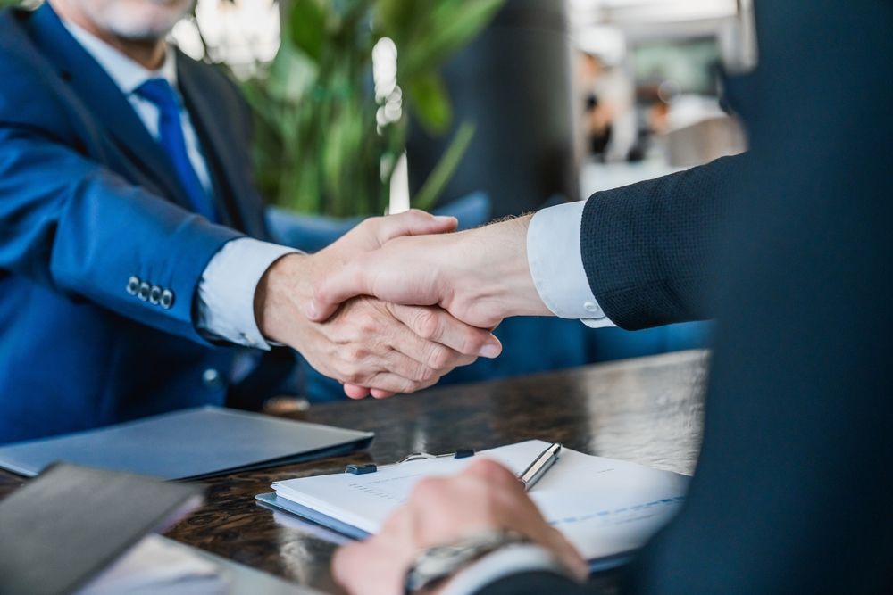 Two businessmen are shaking hands while sitting at a table.