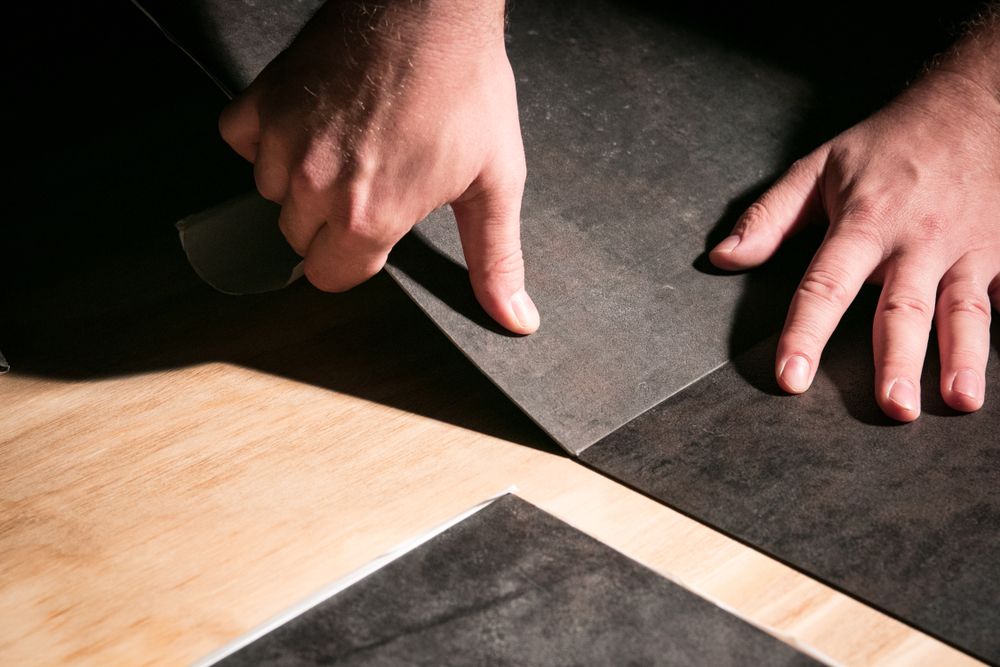 A person is cutting a piece of black vinyl on a wooden floor.