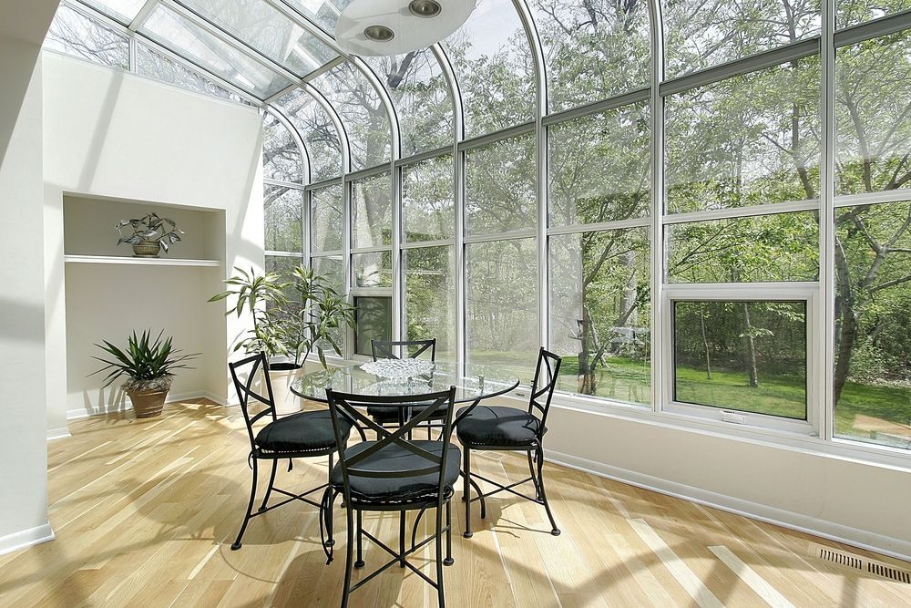 A dining room with a table and chairs and lots of windows.