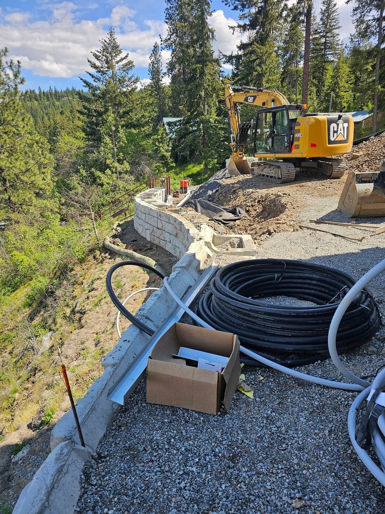 Construction site with retaining wall, excavator, and building materials outdoors on a hillside.