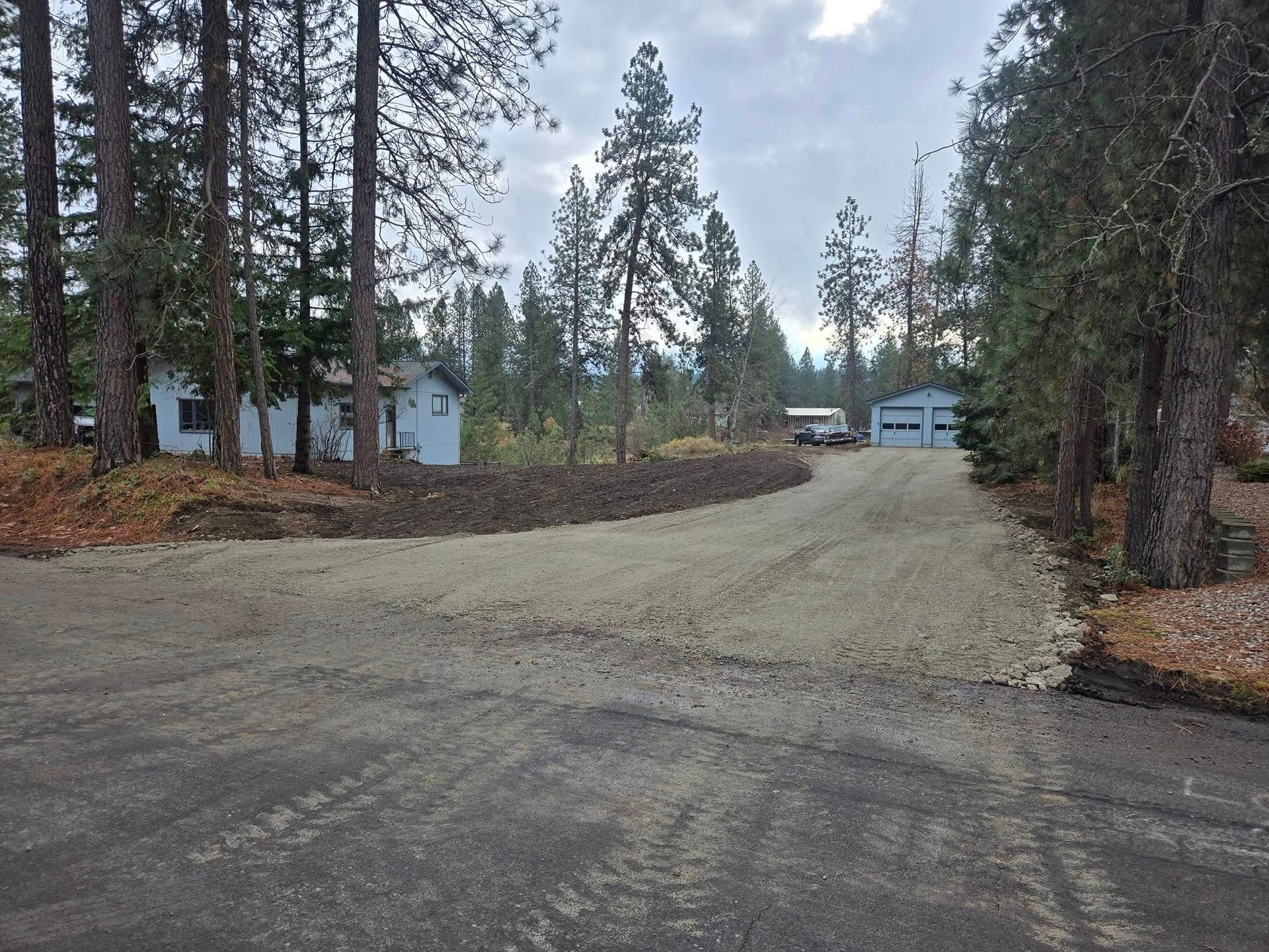 Gravel driveway leading to two houses with trees in a rural setting.
