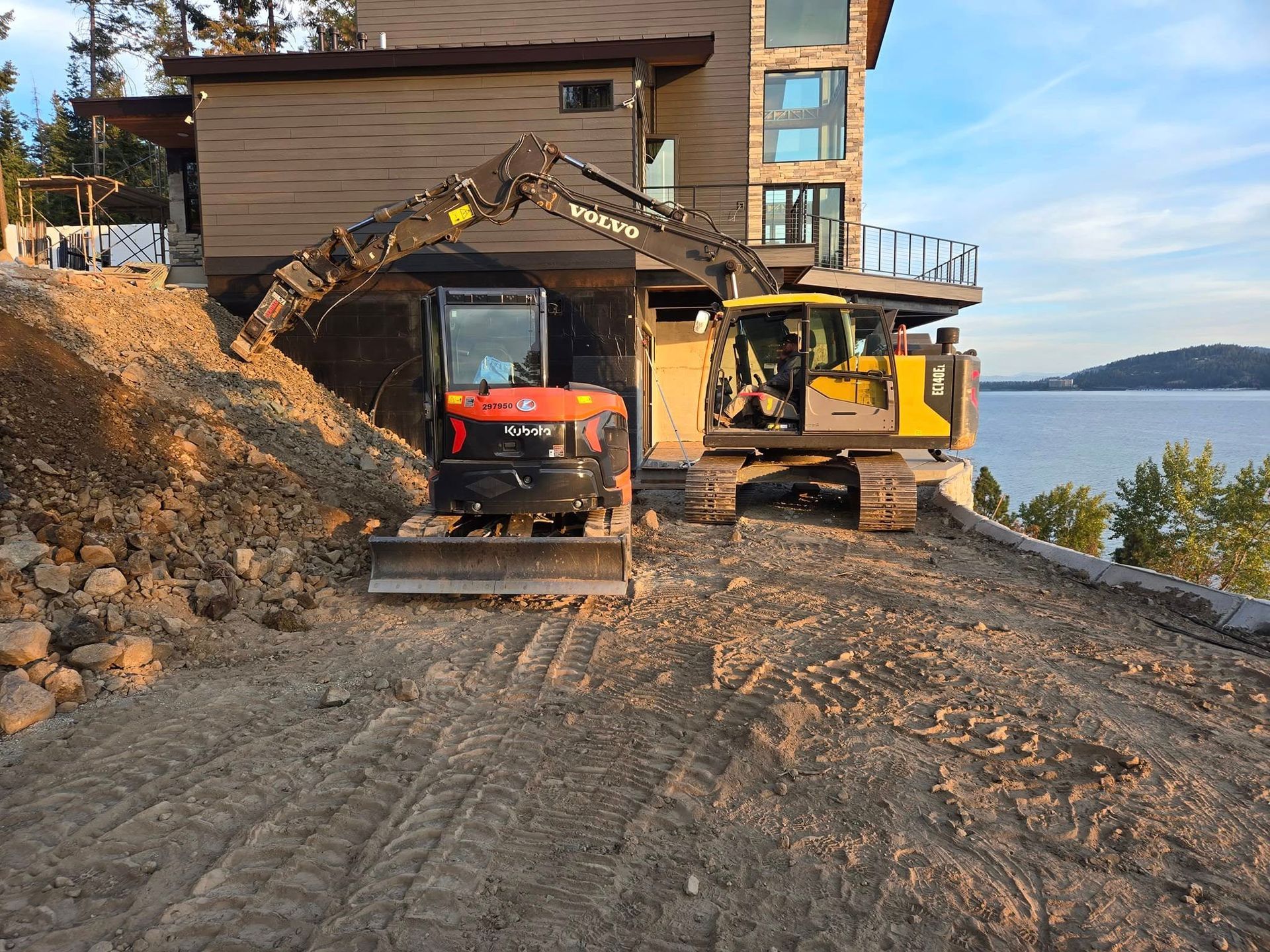 Excavators on a construction site near a waterfront home; digging earth.