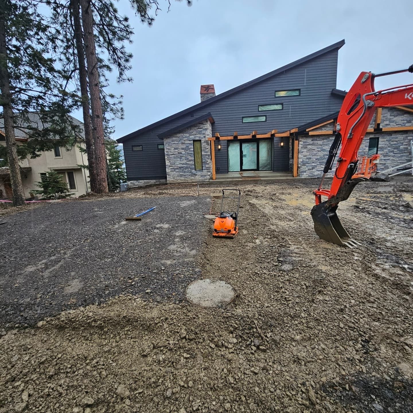 A modern home under construction with an excavator and soil compactor.