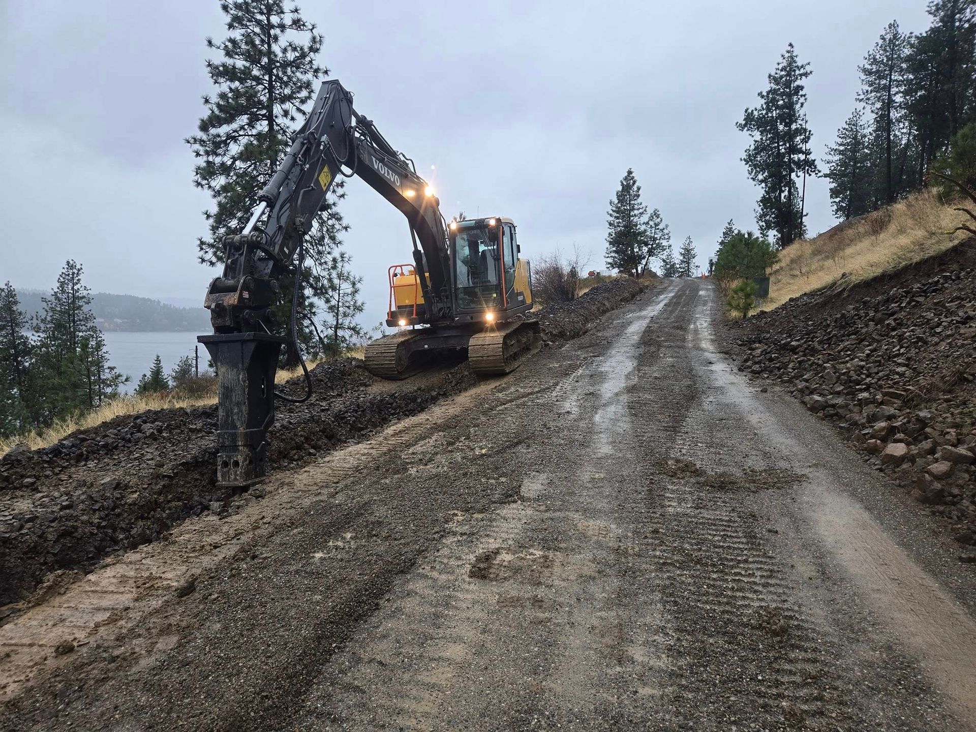 Excavator on a gravel road, working on a hillside. Overcast sky.