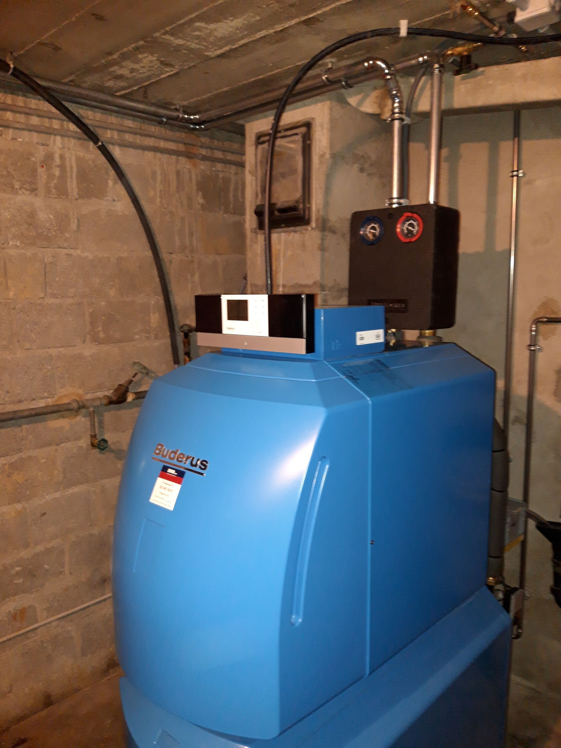 Une chaudière bleue se trouve dans un sous-sol à côté d'un mur de briques.