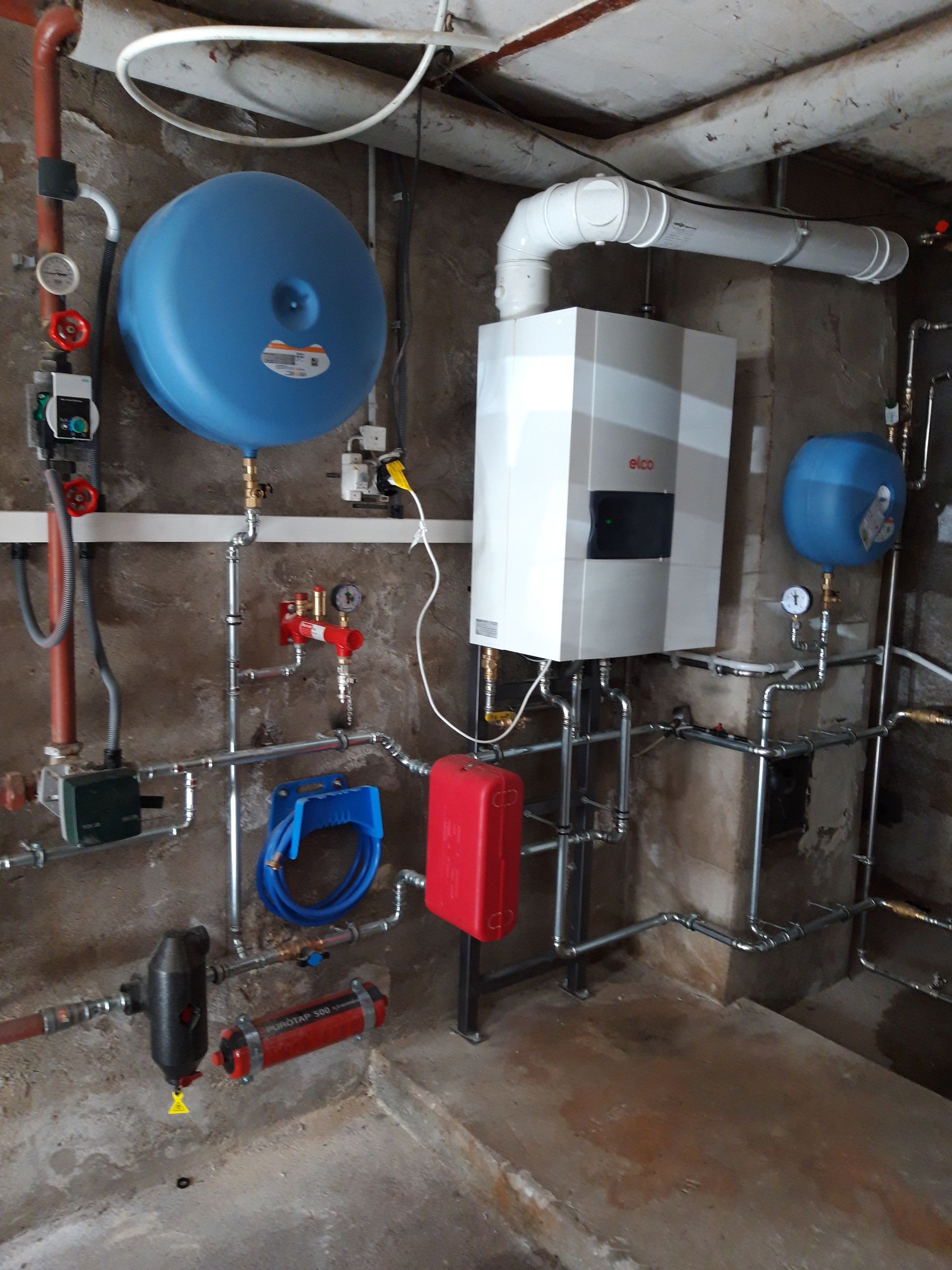 Une pièce avec une chaudière et un réservoir bleu au mur