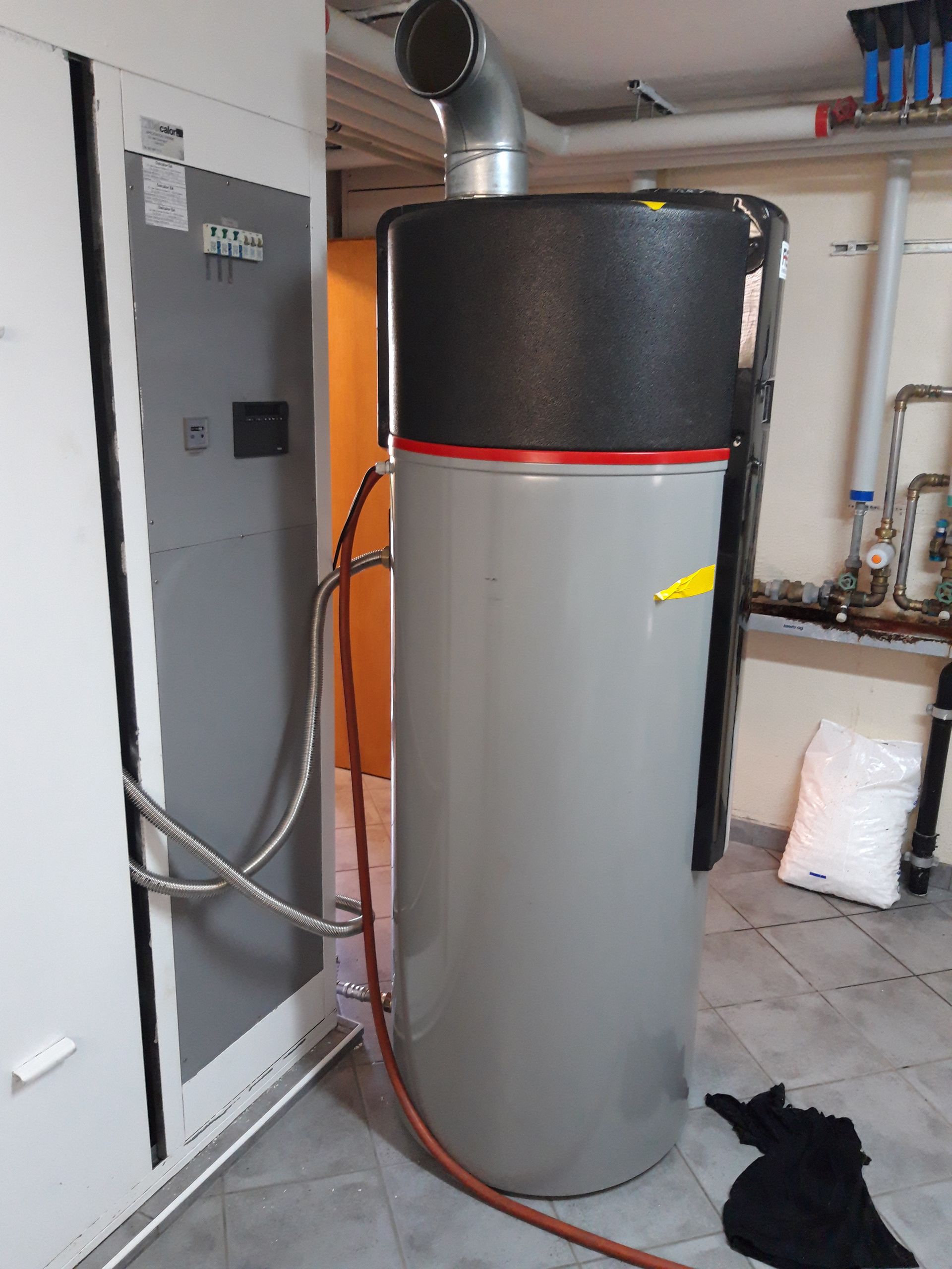 Un grand chauffe-eau grise est raccordé à un tuyau dans une pièce.