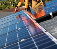 Un homme installe des panneaux solaires sur le toit d'une maison.