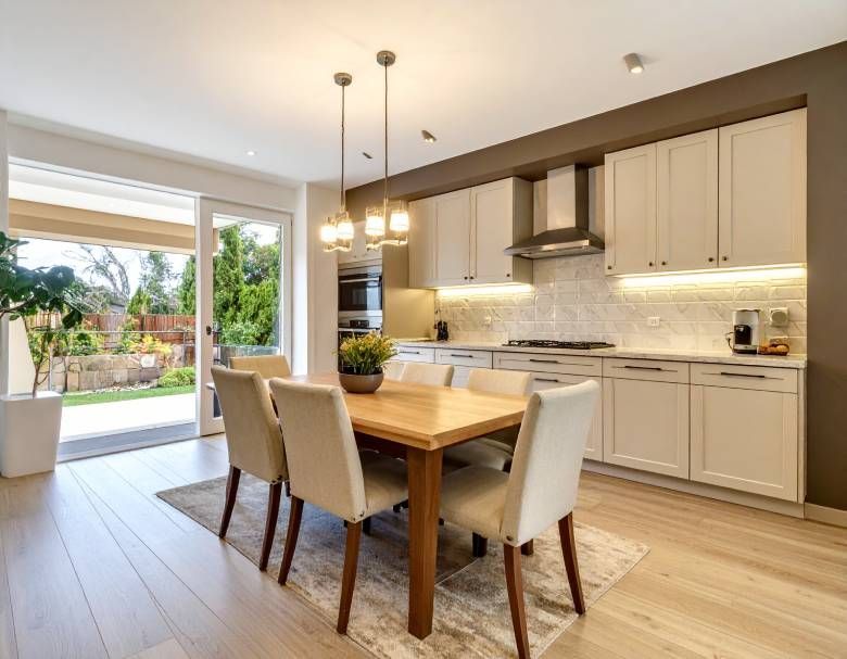 Modern kitchen with dining area, light wood floor, cream cabinets, and a table with six chairs.