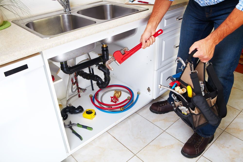 A Man Is Fixing A Sink In A Kitchen With A Wrench — Blueline Plumbing Services in Browns Plains, QLD