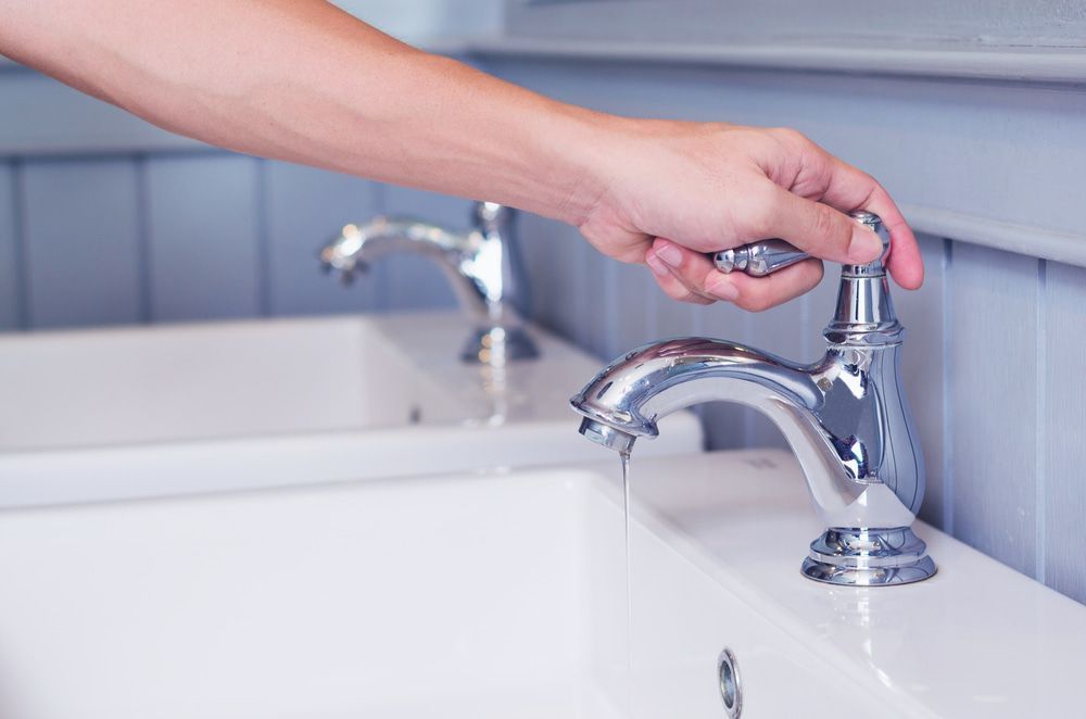 A Person Is Turning On A Bathroom Sink Faucet — Blueline Plumbing Services in Loganlea, QLD