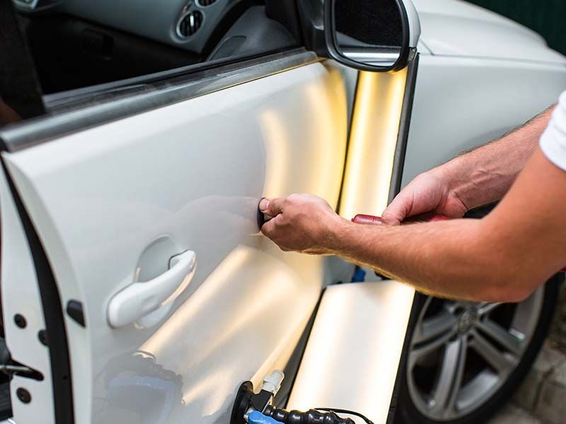 A man is repairing a car door with a tool.