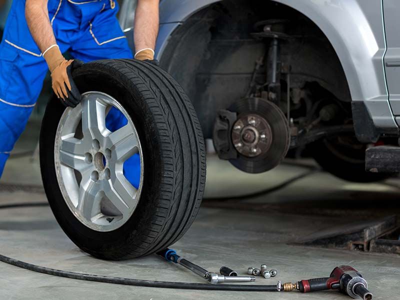 A man is changing a tire on a car in a garage.