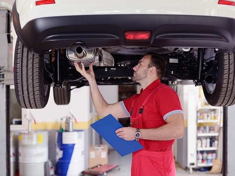 A man is working on the exhaust pipe of a car in a garage.