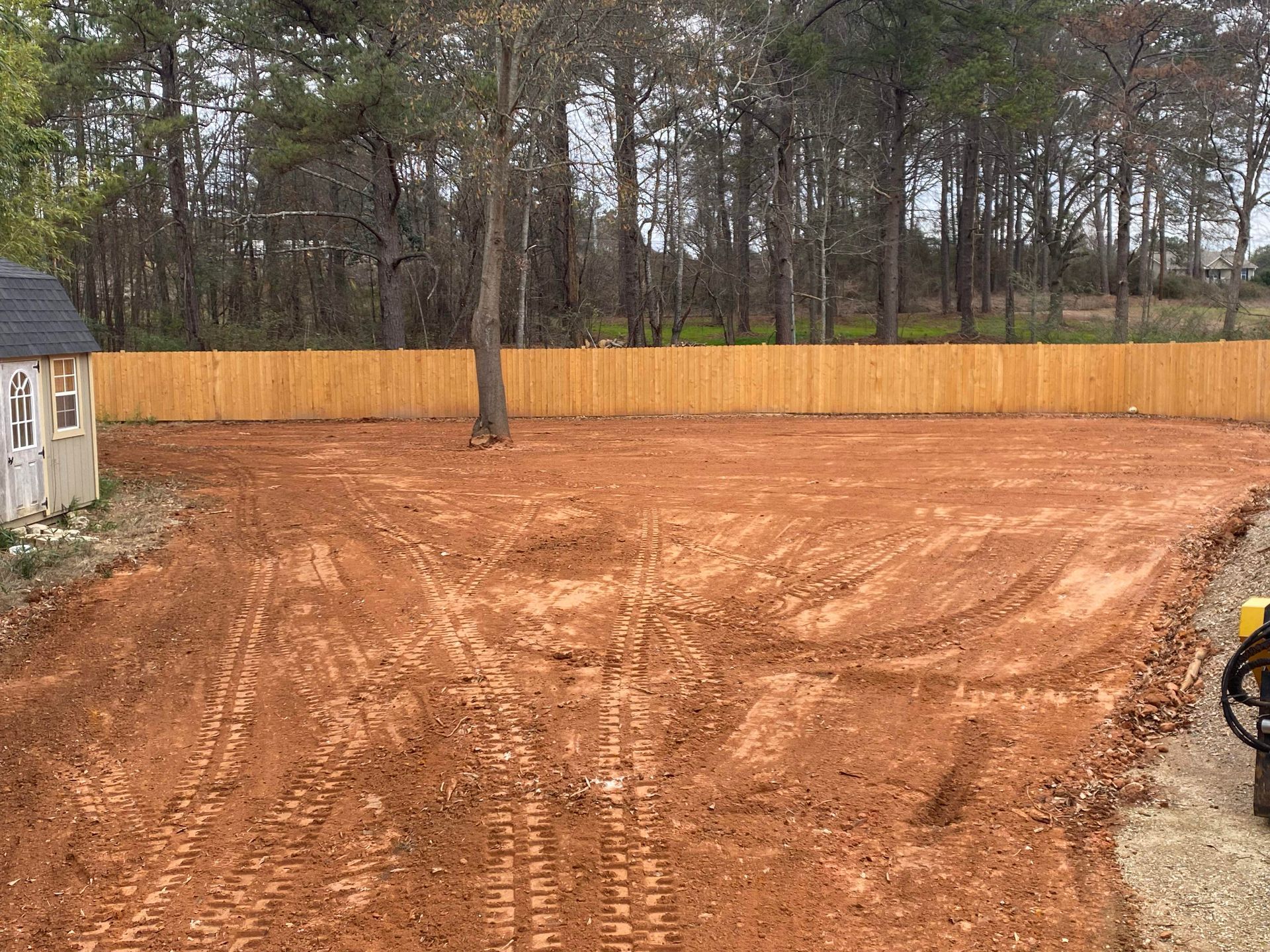 A dirt field with a wooden fence and a shed in the background.