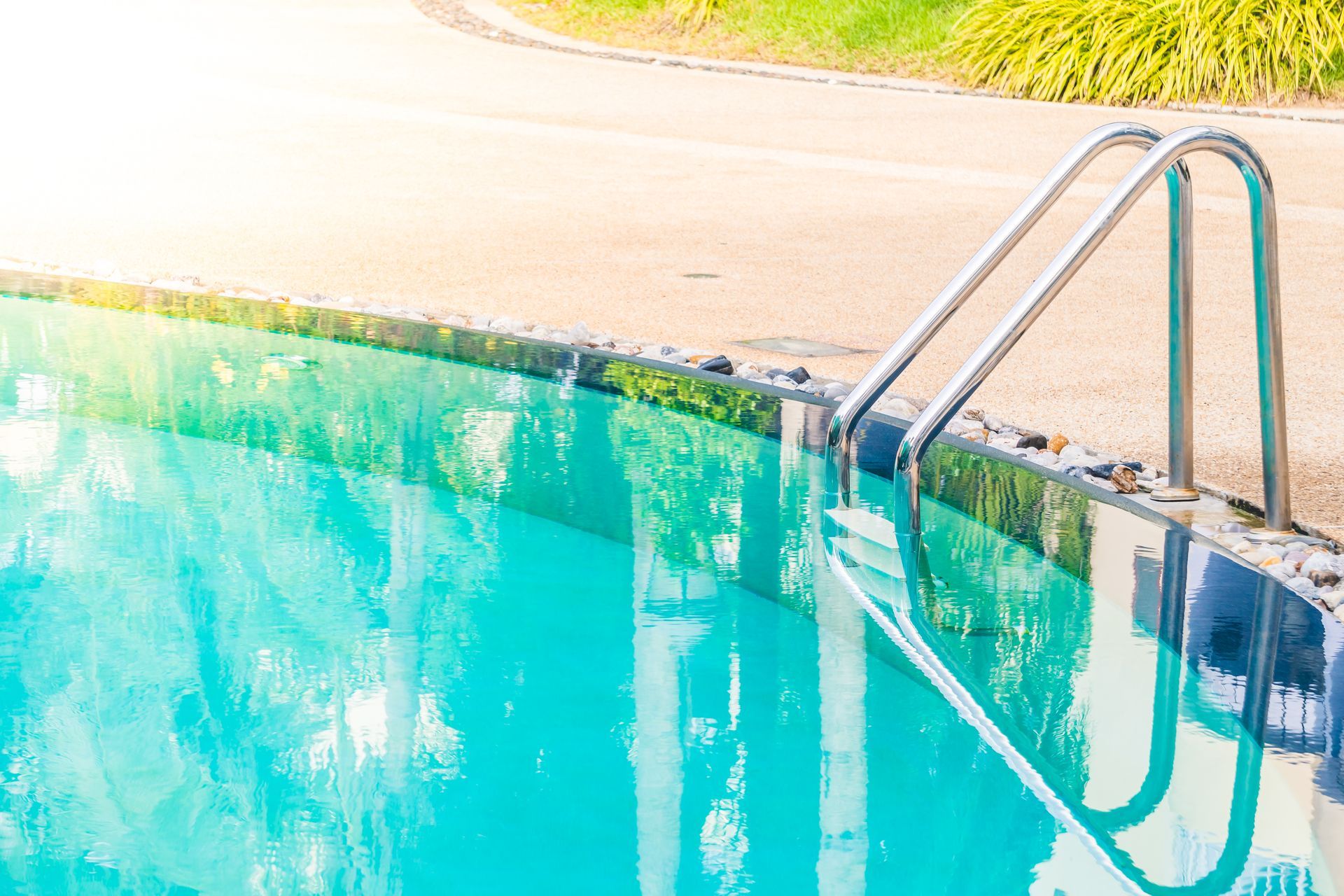Turquoise swimming pool with metal ladder beside a sunlit deck
