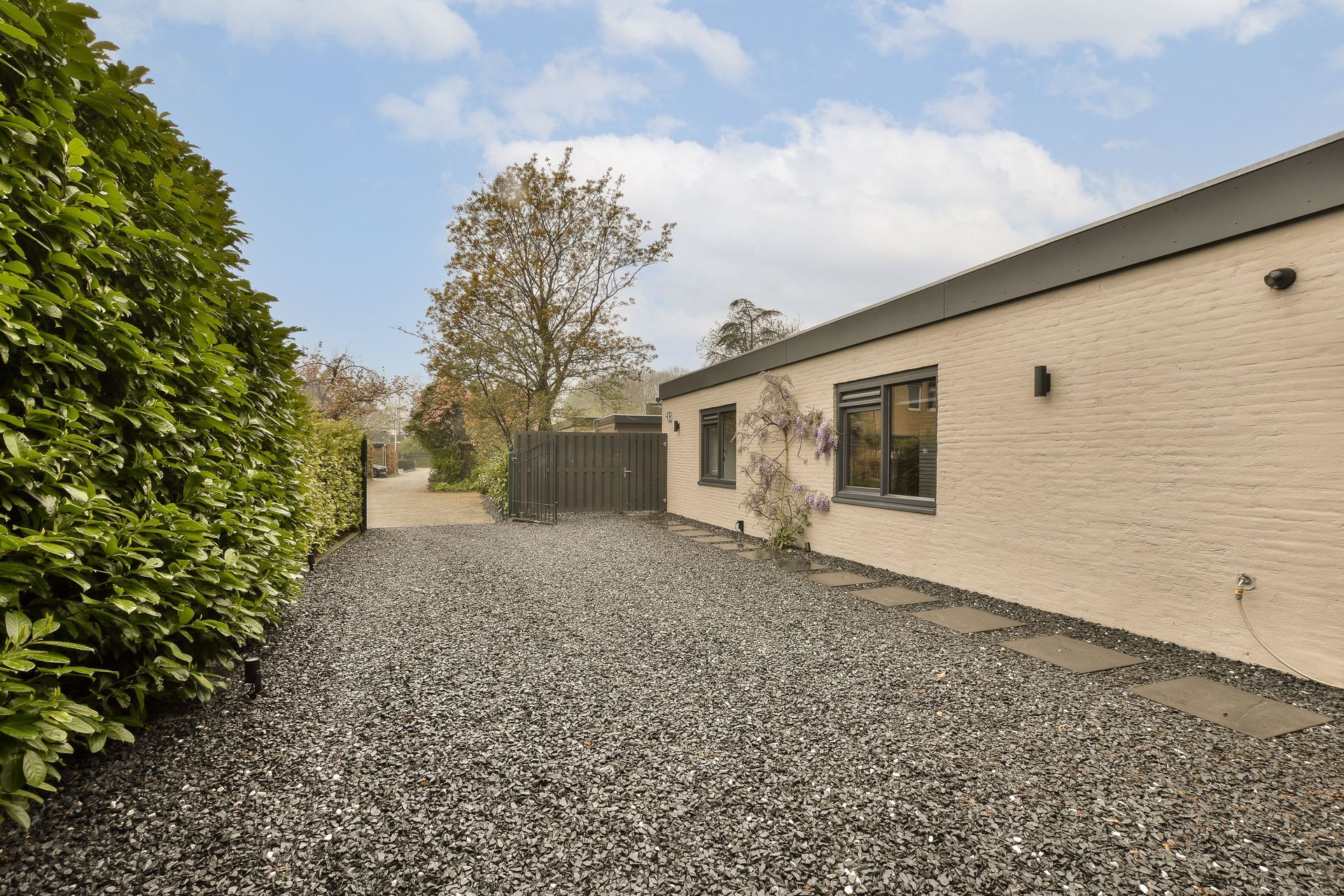 Gravel courtyard beside a cream brick house with windows and a hedge on the left