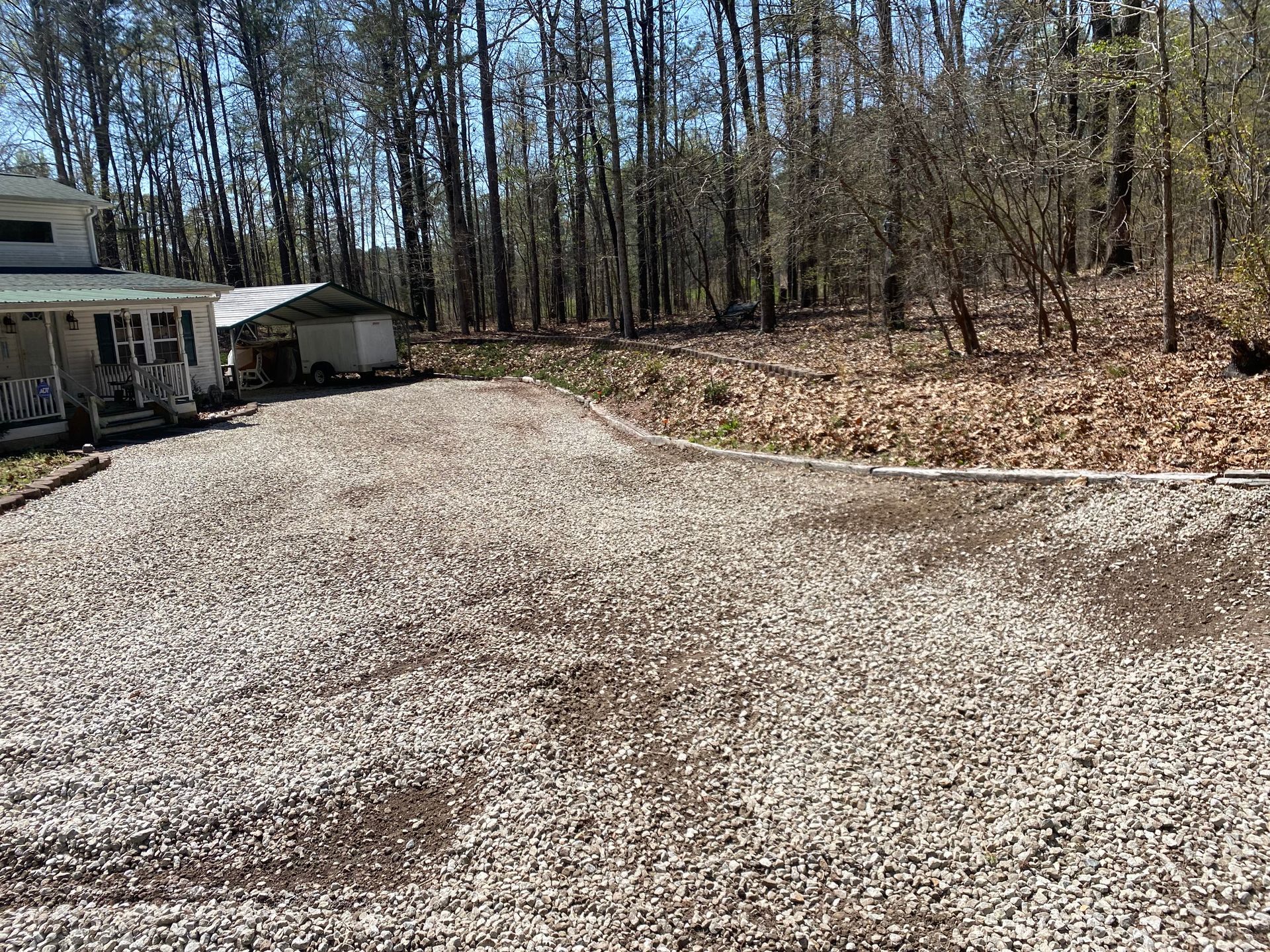 A gravel driveway leading to a house in the woods.