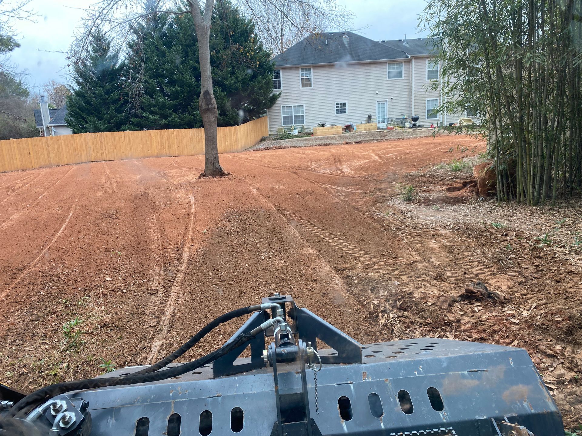 A tractor is driving through a dirt field in front of a house.