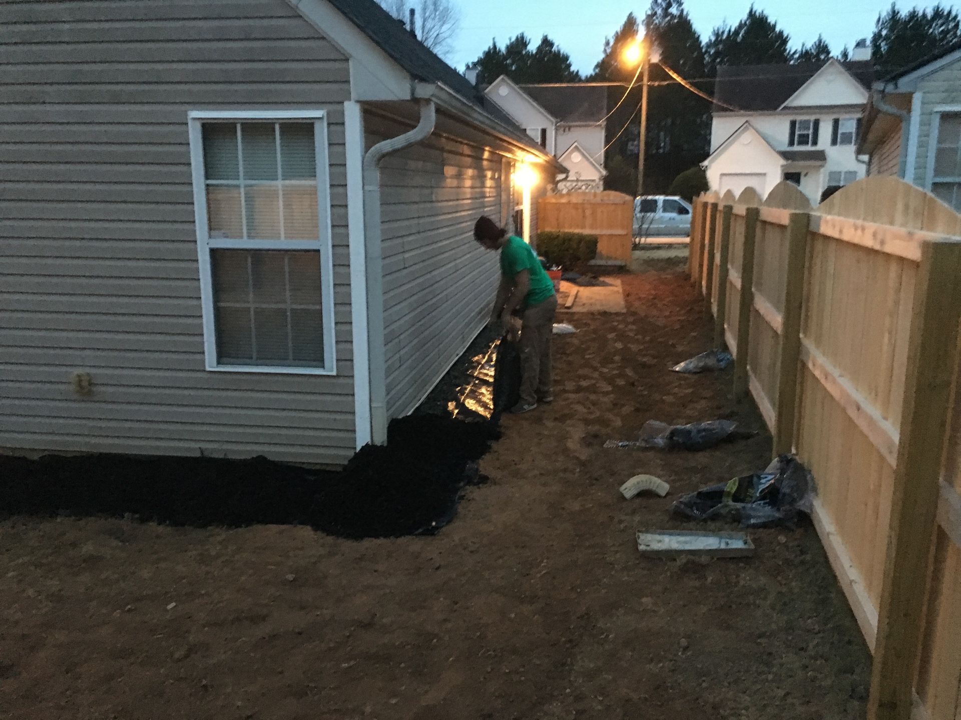 A man is standing next to a wooden fence in front of a house.