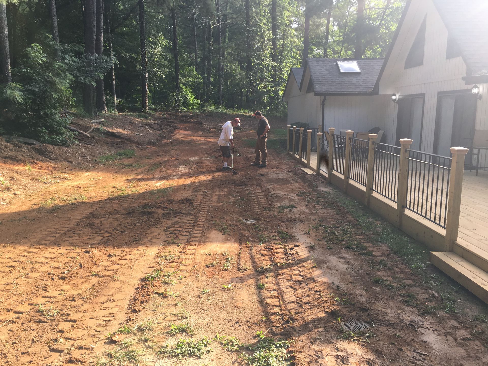 Two men are standing on a dirt road in front of a house.