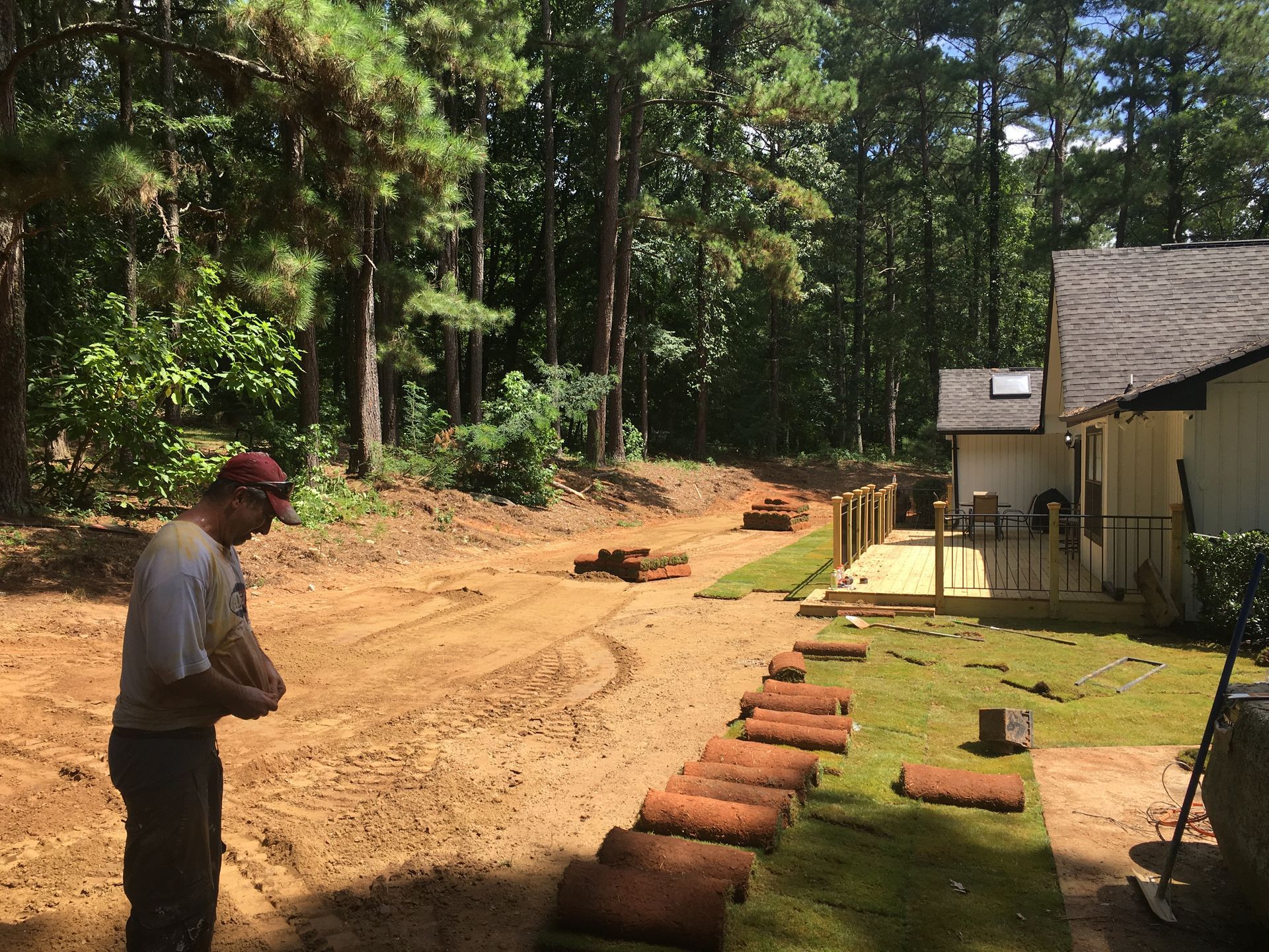 A man is standing on a dirt road next to a house.