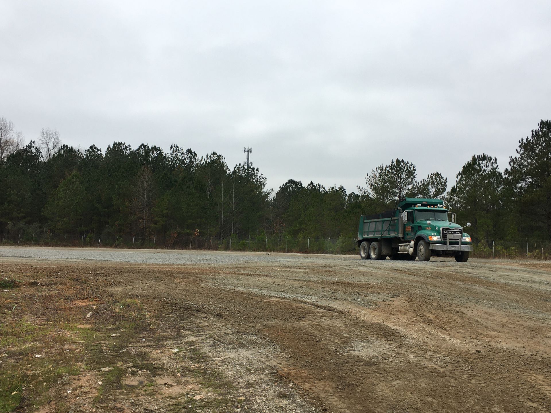 A green dump truck is driving down a dirt road.