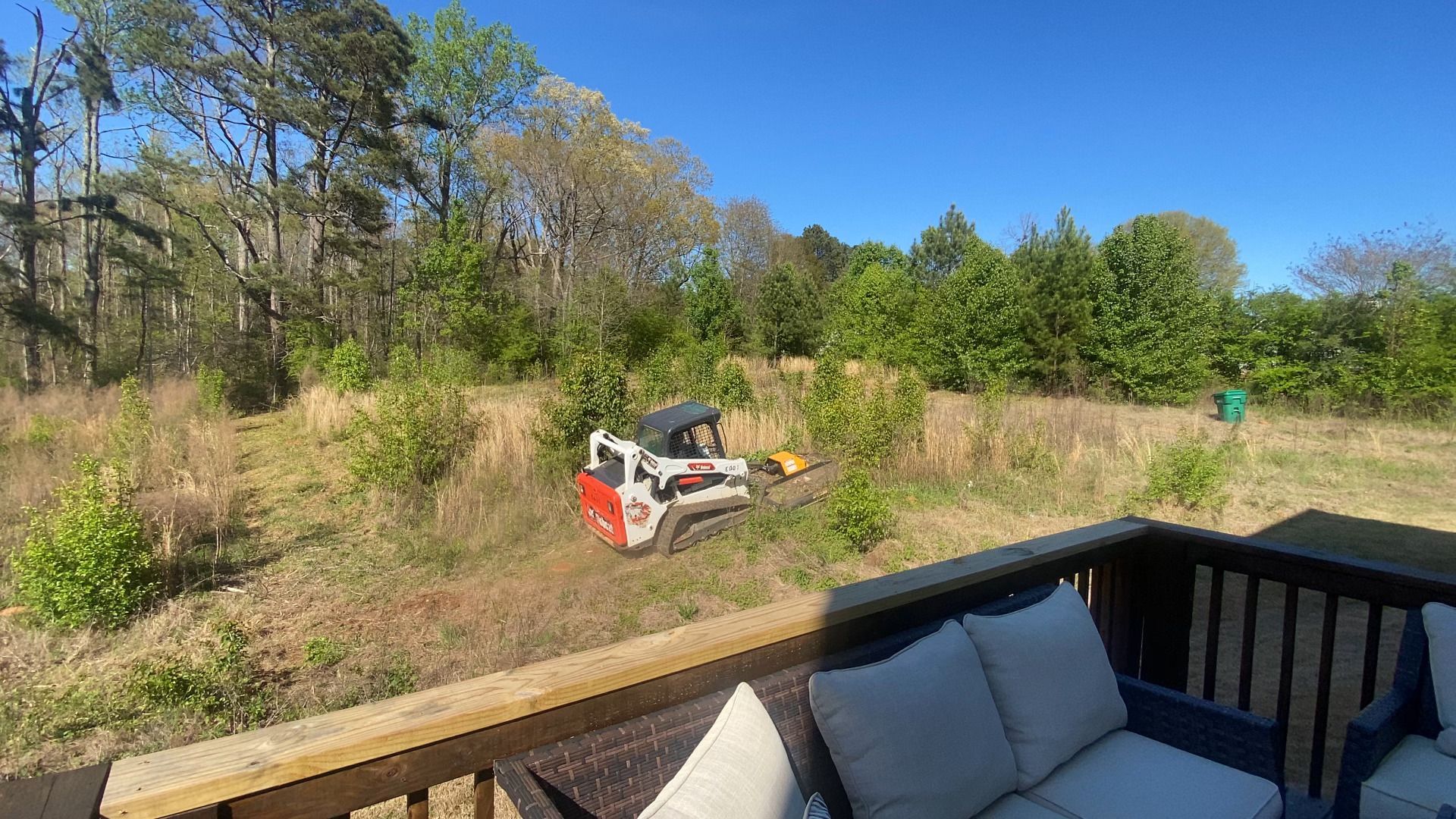 A bulldozer is driving through a field next to a couch on a deck.