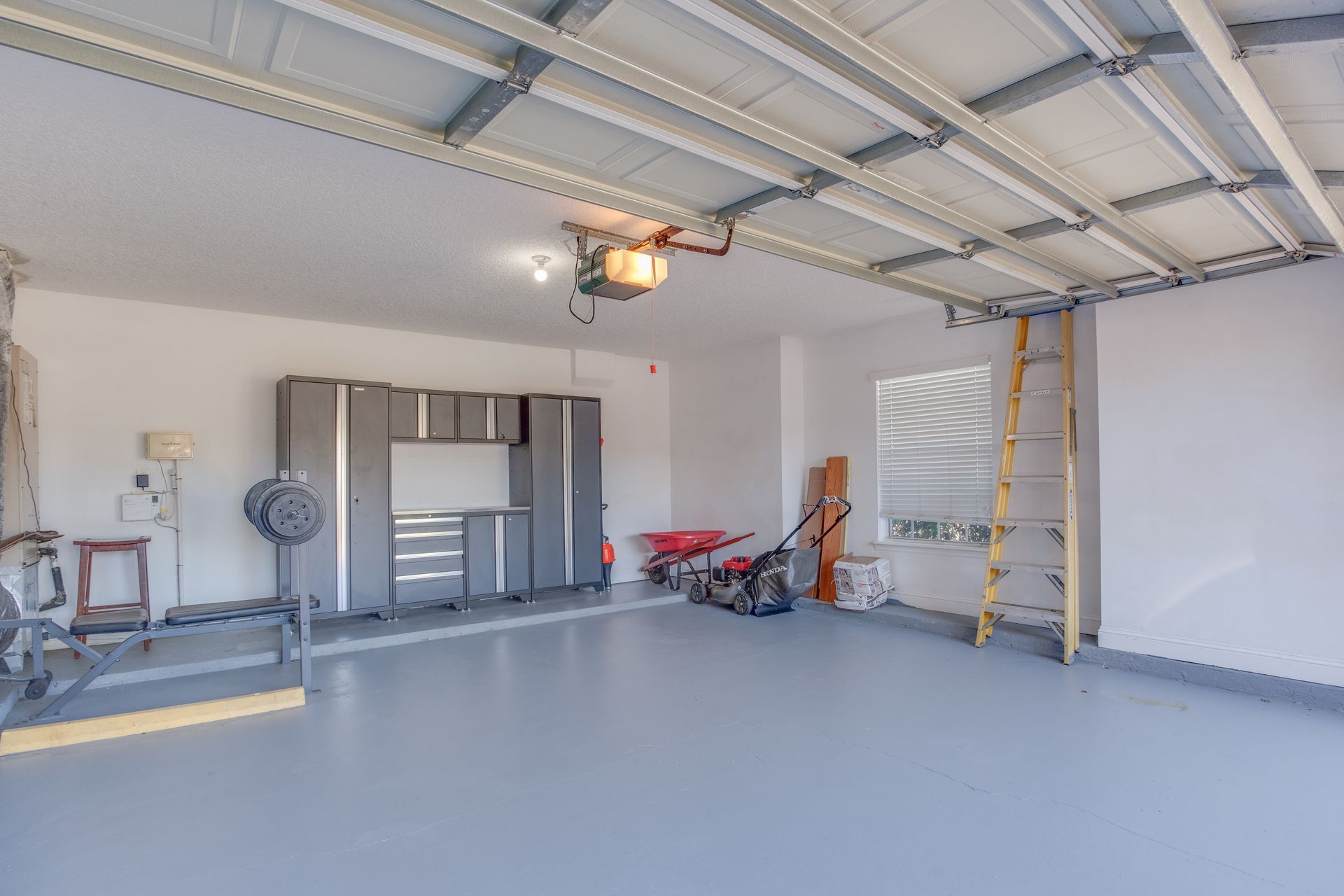 Empty garage with gray floor, cabinets, and a lawnmower.
