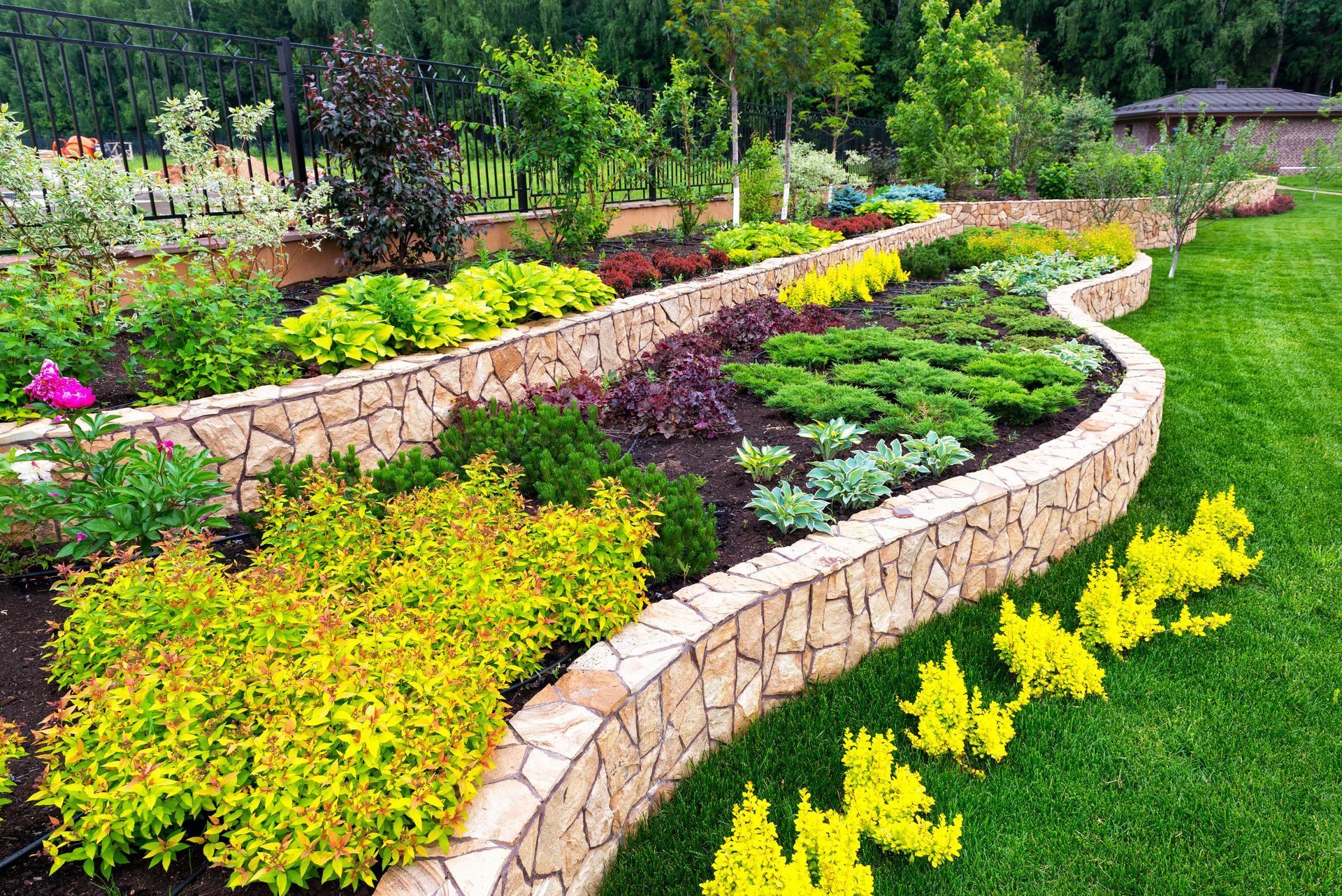 Multi-tiered garden bed with stone walls, filled with colorful plants and vibrant green grass.