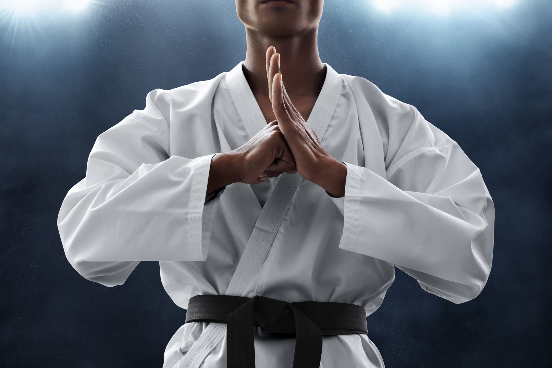 Persona in uniforme da karate, mani giunte in un inchino, cintura nera, sfondo scuro, riflettore.
