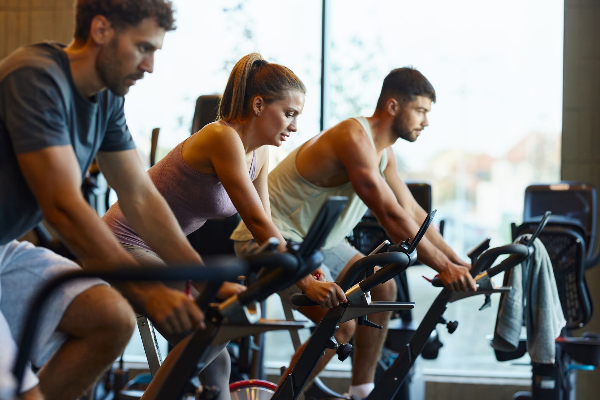 Tre persone, due uomini e una donna, pedalano su cyclette in una palestra.