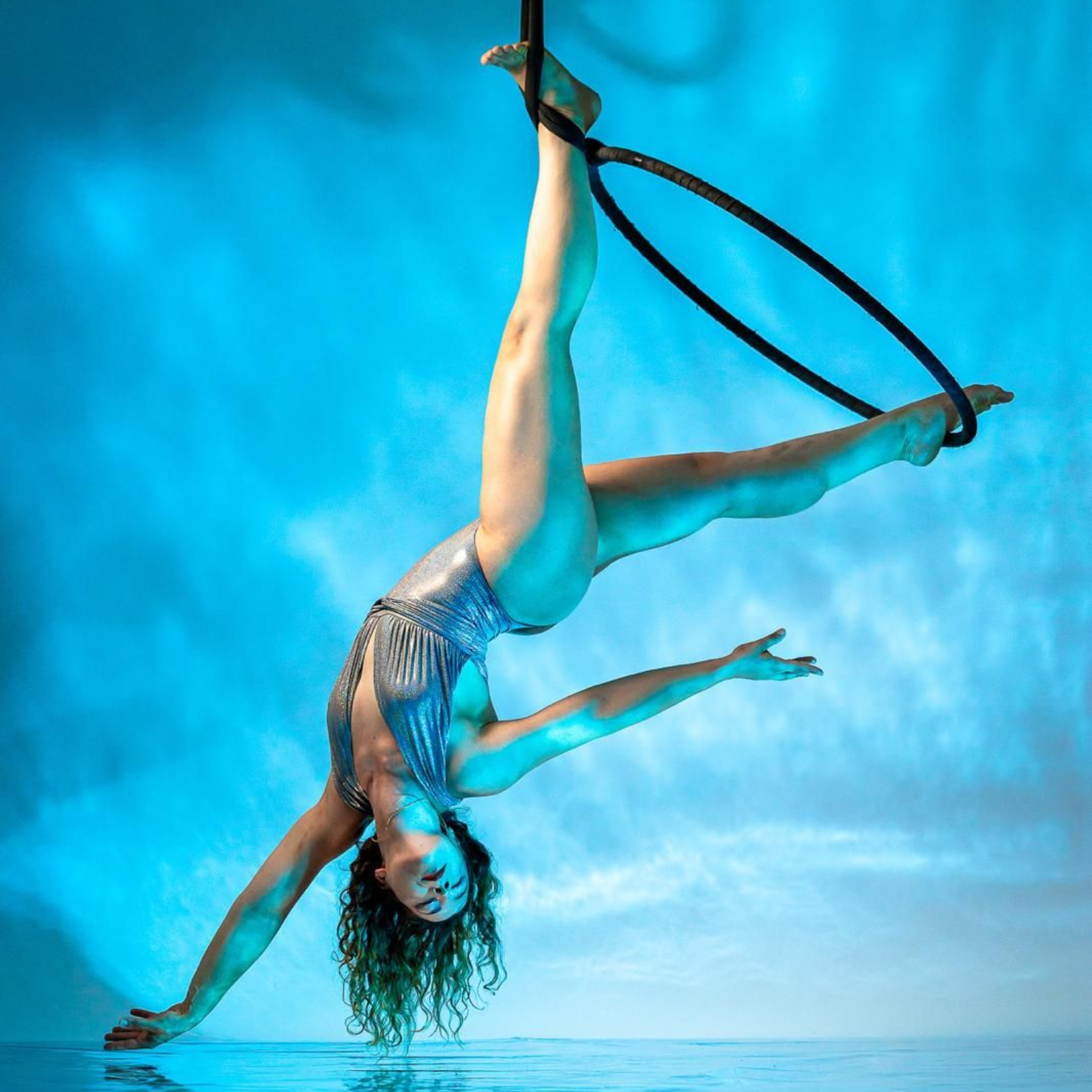 Donna in abito color corallo che si capovolge su un cerchio aereo in uno studio ben illuminato.