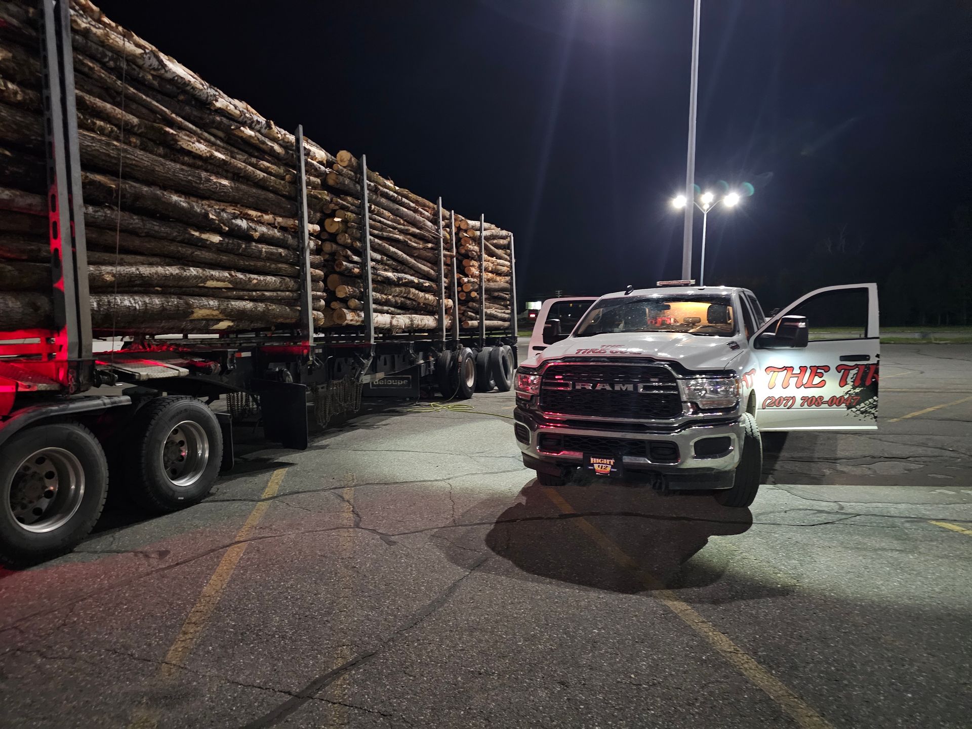A white truck is parked in front of a pile of logs.