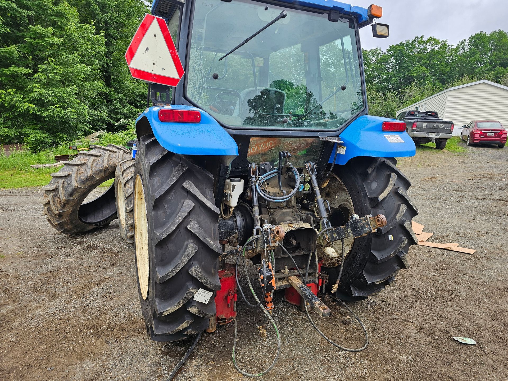 A blue tractor is parked in a dirt lot.